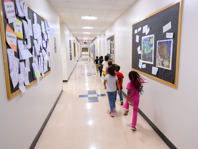 Young school kids walk in a single-file line through a school hallway