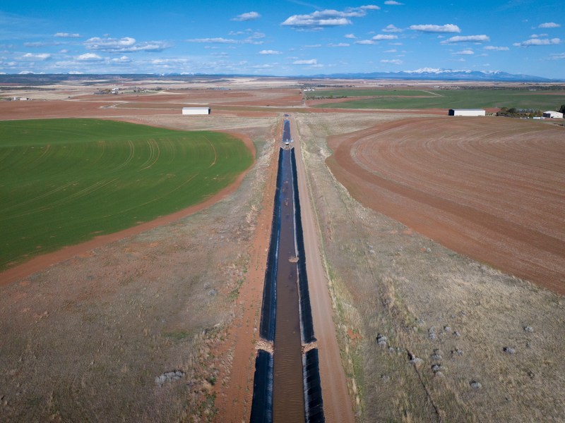 a canal of water through a brown landscape with a green pasture on the left