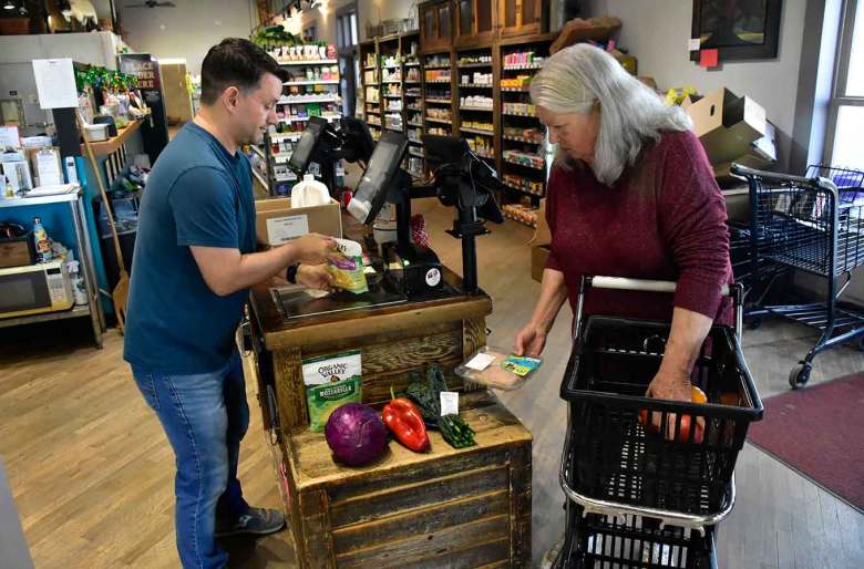 A cashier scans groceries at a checkout counter while a woman holding a shopping basket gets ready to pay at a grocery store.