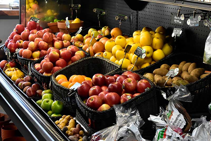 Baskets of apples, kiwis, and other fruits are displayed on shelves in the produce section of a grocery store.