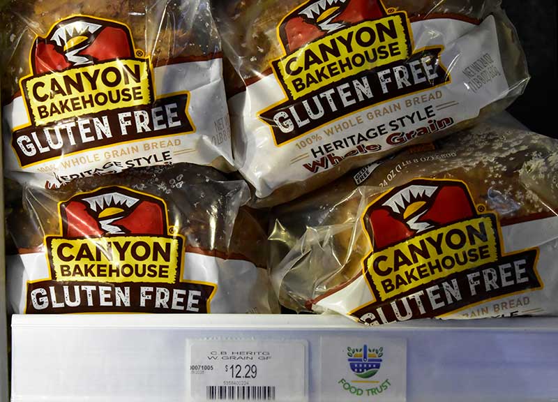 Four loaves of Canyon Bakehouse gluten free bread are displayed on a store shelf, with a price tag reading $12.29 below them.
