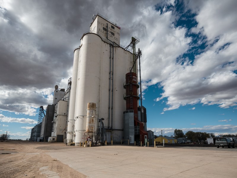 A large white grain elevator in northeastern Colorado stands against bright blue sky streaked by moody clouds