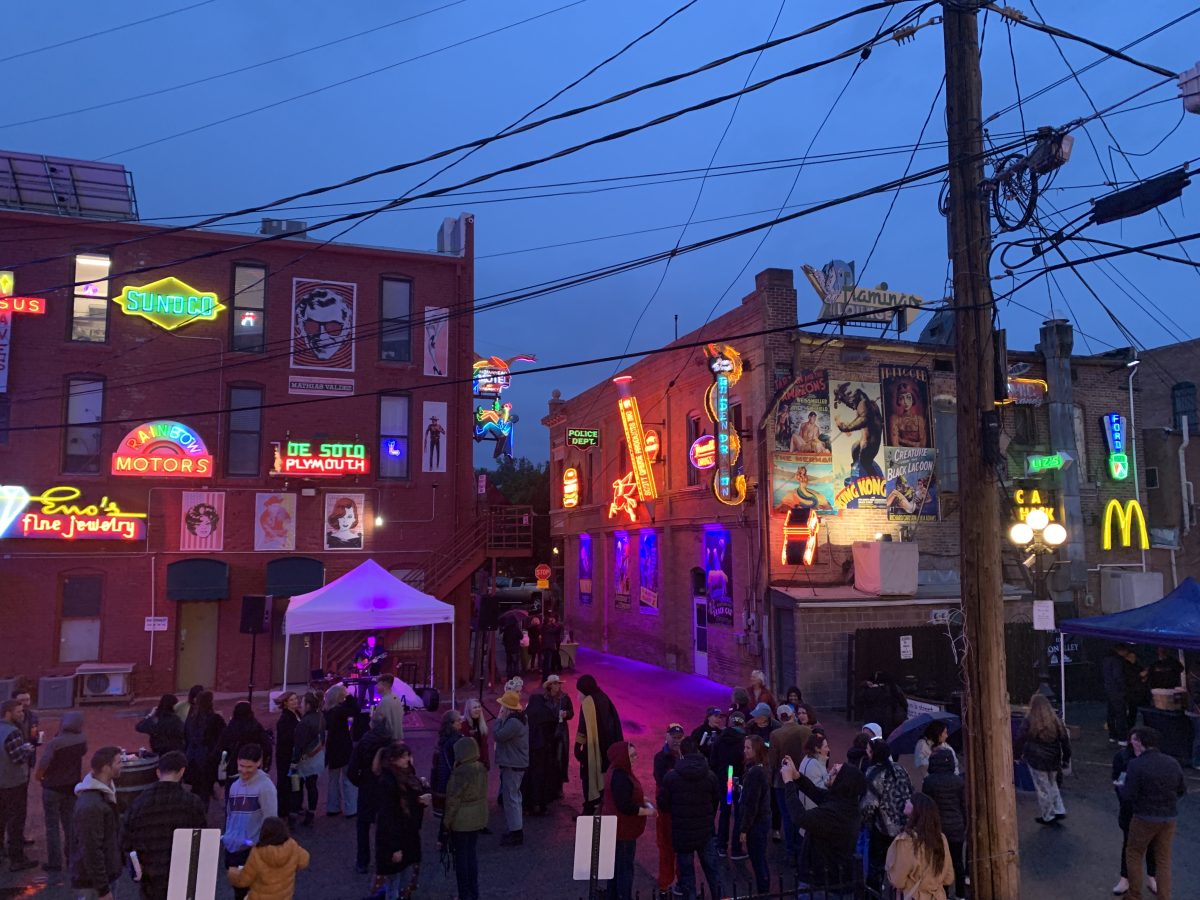 Vibrant street scene at dusk with people gathered, neon signs illuminating bars and shops, and a lively atmosphere in an urban setting.