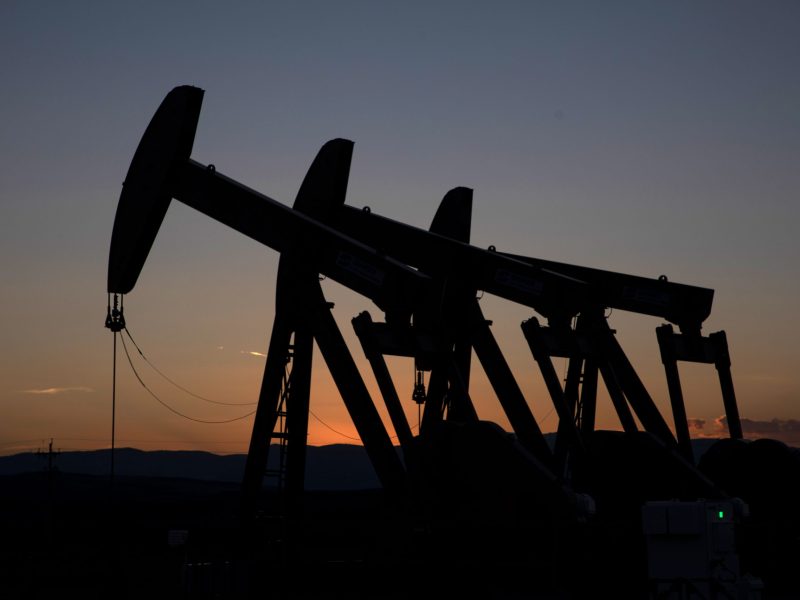 Silhouetted oil pump jacks against a sunset sky, with hills in the background.