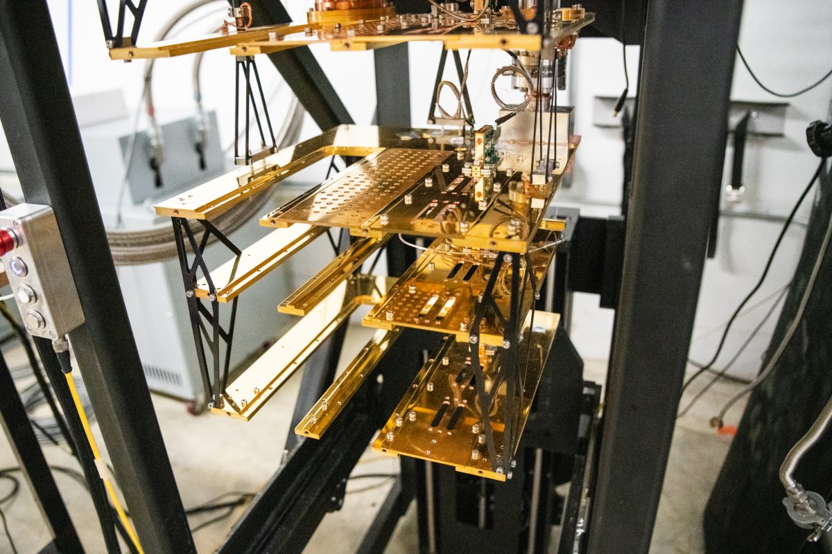 Close-up of a quantum computer's internal structure, displaying multiple gold-plated shelves with intricate wiring and components, in a laboratory setting.