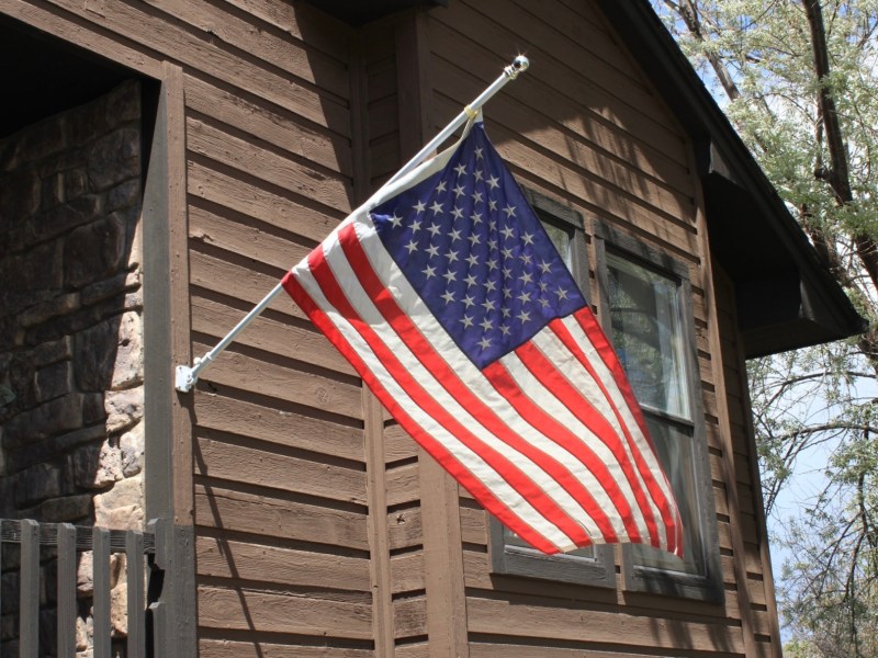 An American flag flying near the front door of a brown house.