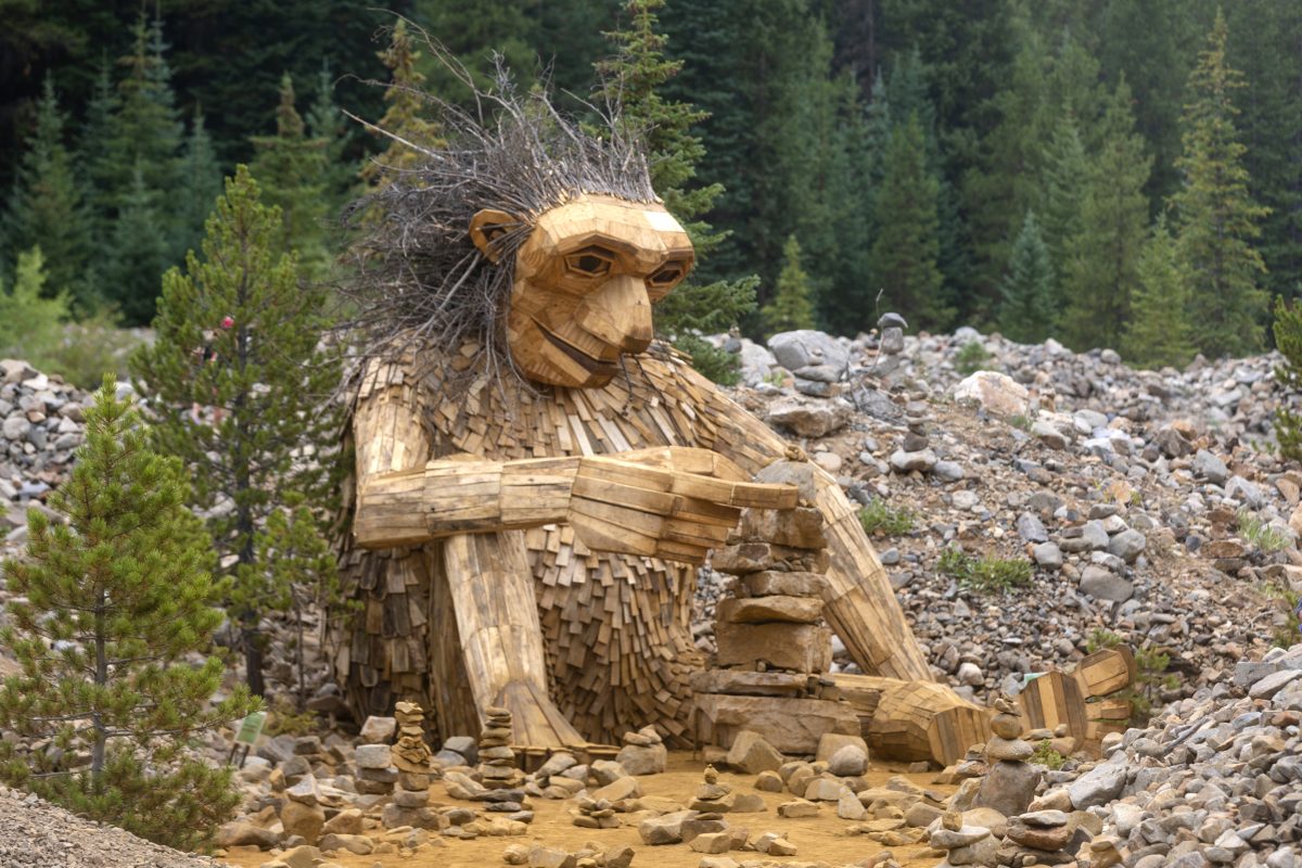 a large wooden troll is seen stacking rocks surrounded by pile of rocks